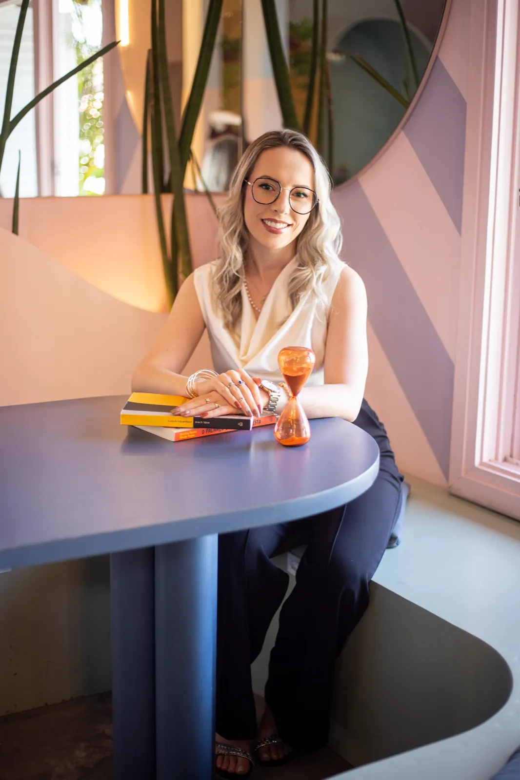 Daniela Bézi sentada à mesa, com livros e uma ampulheta